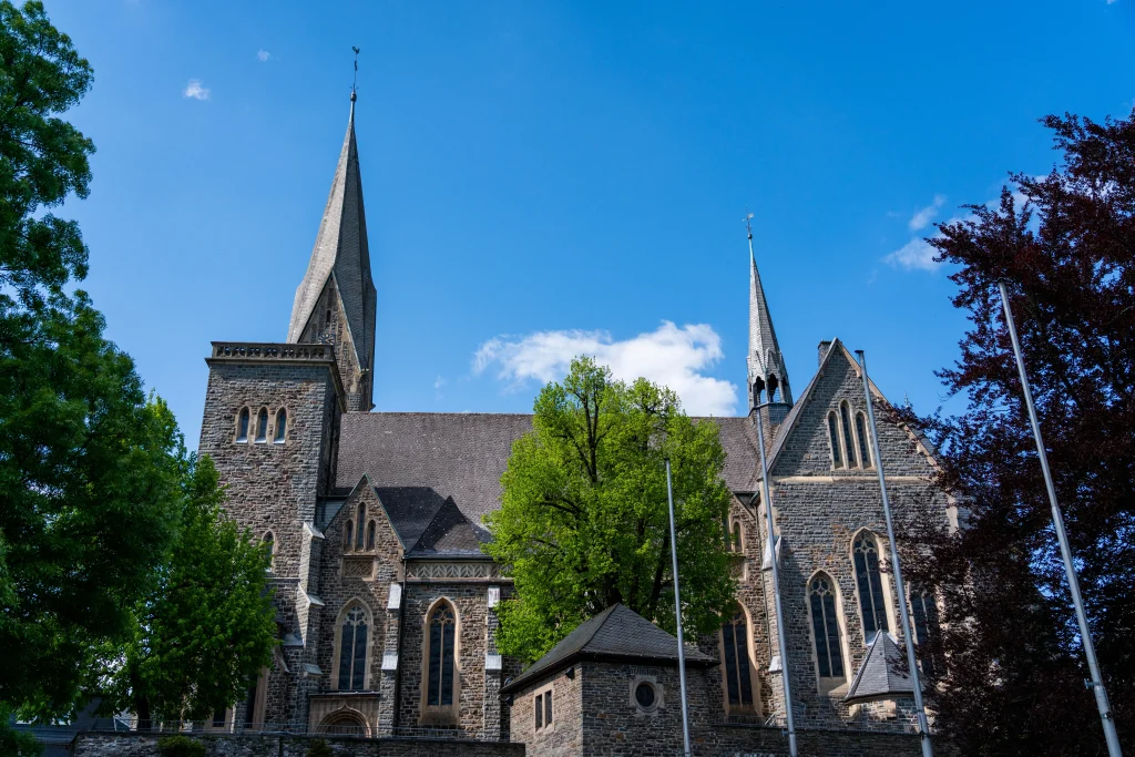 Neugotische St.-Martinus-Kirche in Olpe aus Naturstein mit markantem Turm unter blauem Sommerhimmel